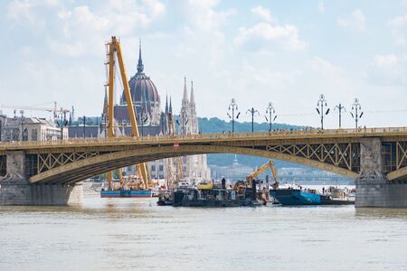 Budapest, Hungary - June 09 2019: Crane and work boats operating at the site of an accident where two boats collided under the Margaret Bridge with the Hungarian Parliament Building in the background.のeditorial素材