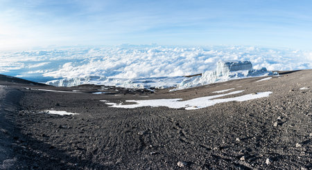 Footprints lead off through volcanic ash and dust towards a glacier sitting above the clouds on the...