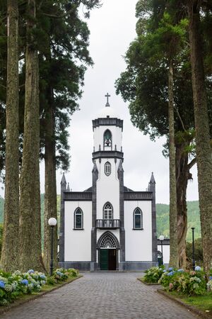 Sete Cidades, SÃ£o Miguel Island, Azores - September 04 2019: View of the Church of SÃ£o Nicolau in the town of Sete Cidades. The path leading to the revivalist Neo-Gothic church is lined by trees.のeditorial素材