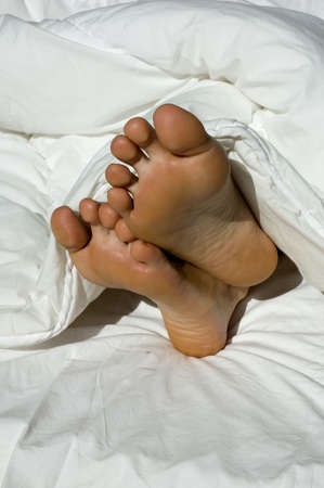 A couple of feet sticking out of a feather duvetの写真素材