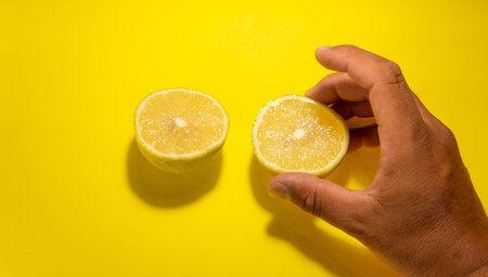 two lemon cut into slices on yellow background holding it by the handの写真素材