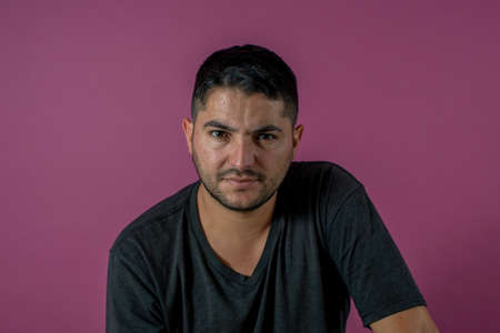 serious looking camera eyes, young brunet man, 20s, wears blue shirt looking at camera smiling isolated on light pink background studio portrait. People emotions lifestyle conceptの写真素材
