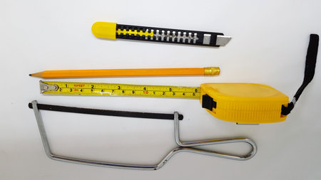 A collection of woodworking tools including a Junior hacksaw, A small utility knife, a yellow pencil and a yellow tape measure.の写真素材