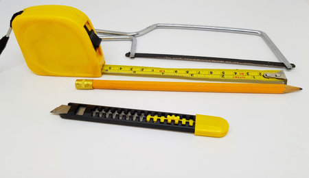 A collection of woodworking tools including a Junior hacksaw, A small utility knife, a yellow pencil and a yellow tape measure.の写真素材