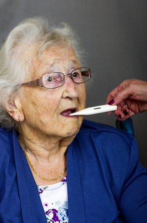 Senior lady having a temperature check with a digital thermometer by a health care worker.の写真素材