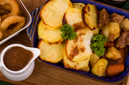 Beef in Irish Stew. A dish of Beef with a topping of sliced potatoes, served with a selection of vegetables and Sourdough bread, with battered onion rings and a jug of onion gravy. A St. Patrickâs Day favourite.の写真素材
