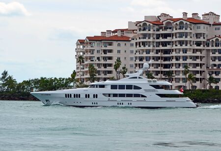 Mega motor yacht cruising by luxury island condos on it's way to the open ocean.の写真素材
