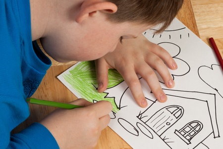 Young boy in blue shirt coloring a picture with pencils while laying on the floor の写真素材