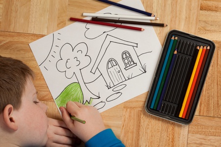 Young boy in blue shirt coloring a picture with pencils while laying on the floor の写真素材