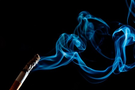 cigarette in front of black background. smoke goes upの写真素材