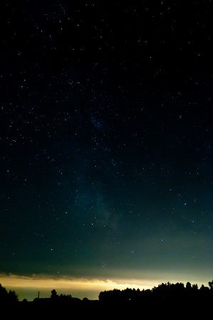 starry sky. clouds at the horizon lighting from the lights from a city. contours are visible from a wood.の写真素材