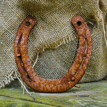 rusty horse shoe leaning against burlap on wood porchの写真素材