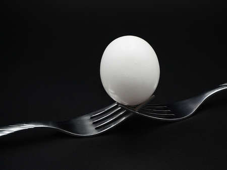 Egg balanced on two forks isolated on black background.の写真素材