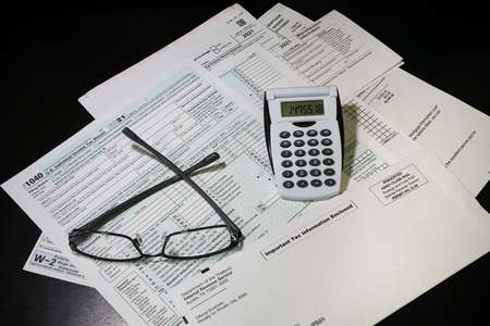 Concept of 2021 Tax preparation documents with eyeglasses and calculator on black background.のeditorial素材