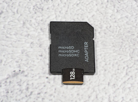 Top view of microSD memory card partially inserted into SD adapter against mottled gray background.