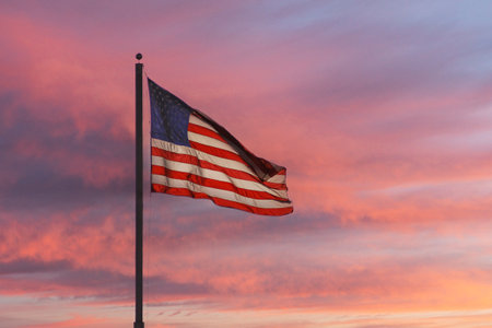 US flag waving with sunset colored clouds in background.の写真素材
