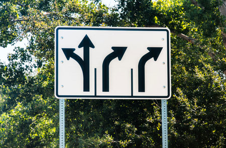 A white traffic sign with black arrows informing motorists of left turn, straight, and right turn lanesの写真素材