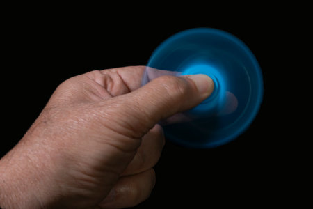 Close up of mans hand holding fidget twist spinner on a black background.の写真素材