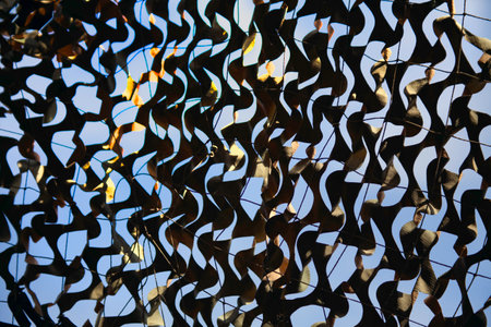 Olive military mesh with torn holes with shadows from bright sunlight. Camouflage net and the blue skyの写真素材