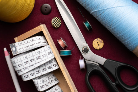 metal scissors, spools, meter, cones and assorted buttons on a dark red fabric