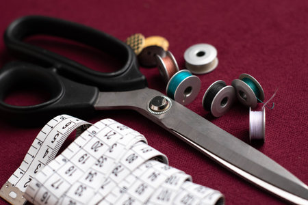metal scissors, spools and white meter on dark red table