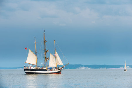 Tall ship on blue water against stormy clouds. Horizontal