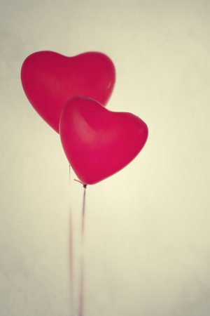 Two red heart's like balloons on soft yellow background.Two red helium balloons, heart shape on soft grey-yellow background, with open space for Valentine's Day text. Vertical.の写真素材