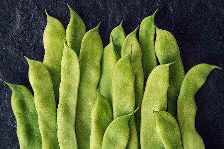 Green flat beans in pods lie on a stone slab. Top view.の写真素材