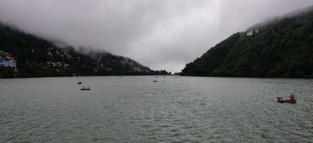 A panoramic shot of a lake surrounded by mountains under a cloudy skyの写真素材