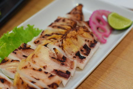 Grilled squid on white plate with lime and onion on wooden table