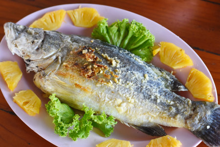 Fried fish with lemon and lettuce on wooden table, Thai foodの写真素材