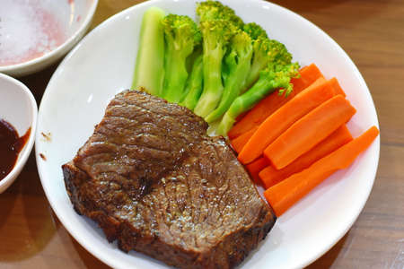 Beef steak with carrot and broccoli in white dish on wooden tableの写真素材