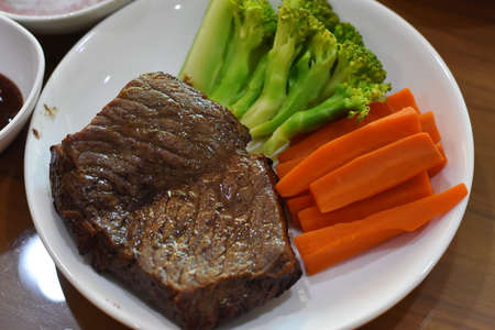 Grilled beef steak with carrot and broccoli on white plate in restaurantの写真素材