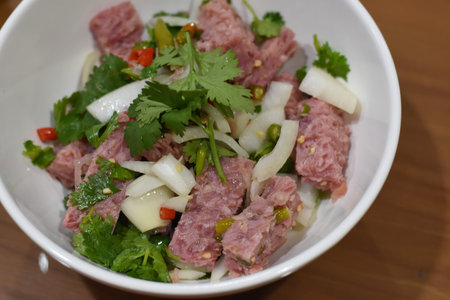 Thai spicy minced pork salad in white bowl on wooden table.