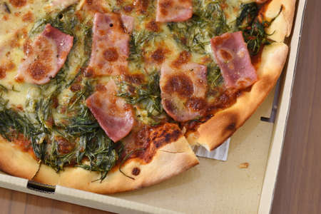 Pizza with ham and spinach in a box on a wooden tableの写真素材