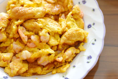 Fried shrimp with scrambled eggs in white plate on wooden table.の写真素材