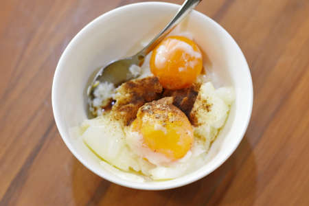 Fried egg with rice and pork in white bowl on wooden tableの写真素材