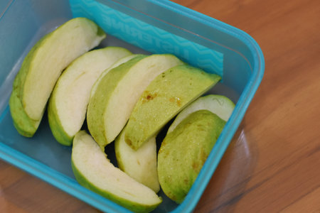 Green guava fruit cut in half in plastic container on wooden table