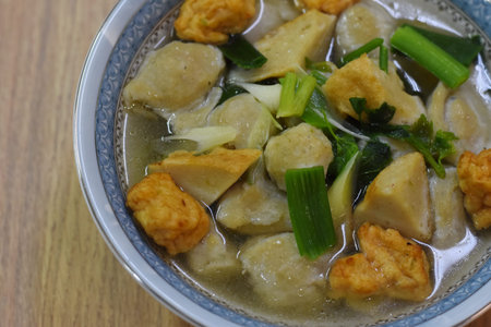 Fried fish ball soup in a bowl on wooden table background.