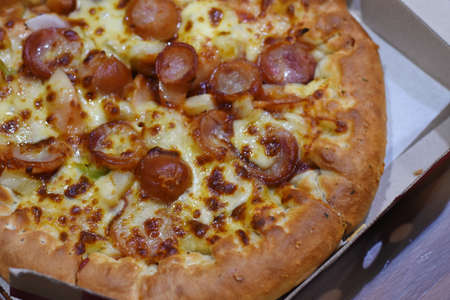 Delicious pizza with sausages and cheese in a cardboard boxの写真素材