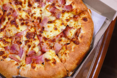 Pizza with ham, bacon and cheese in a cardboard box.の写真素材