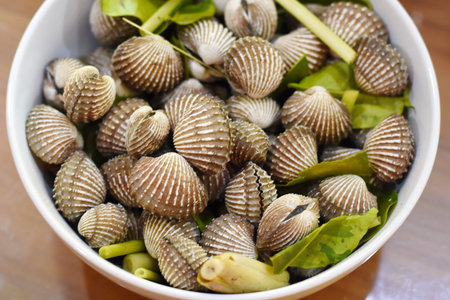 Fresh cockles in white bowl on wooden table, top view.