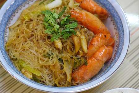 Rice noodles with shrimps and vegetables in a bowl on the table