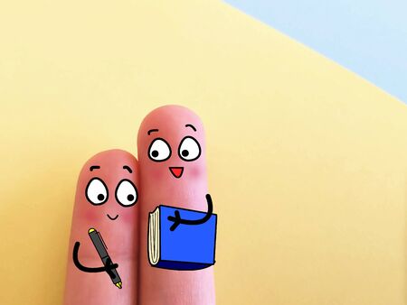 Two fingers are decorated as two person. They are holding a book and a pen.の写真素材