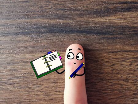 One finger is decorated as a person. The person is holding a pen and a notebook.の写真素材
