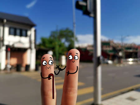 Two fingers are decorated as two person by the roadside. A young man is helping an old man to cross road.の写真素材