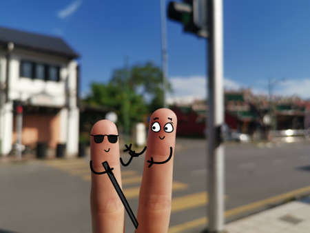 Two fingers are decorated as two person. One of them is helping a blind man to cross road.の写真素材