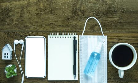 Bottle alcohol spray on white mask, smartphone mock up, notebook blank, Pandemic quarantine work from home concept.の写真素材
