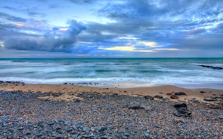 View of a beach with a dramatic storm cloudscape. Image captured at dusk and is a composite of several separate images, with High Dynamic Range (HDR) processing.の写真素材