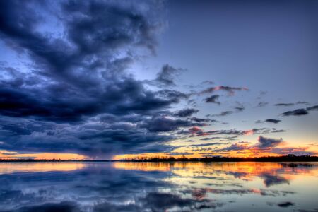View of a rainstorm approaching over a lake, with a setting sun providing an orange glowの写真素材